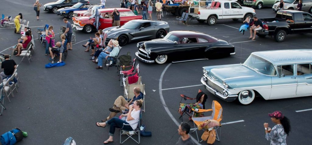 Classic cars at outdoor movie drive-in with people sitting in camping chairs